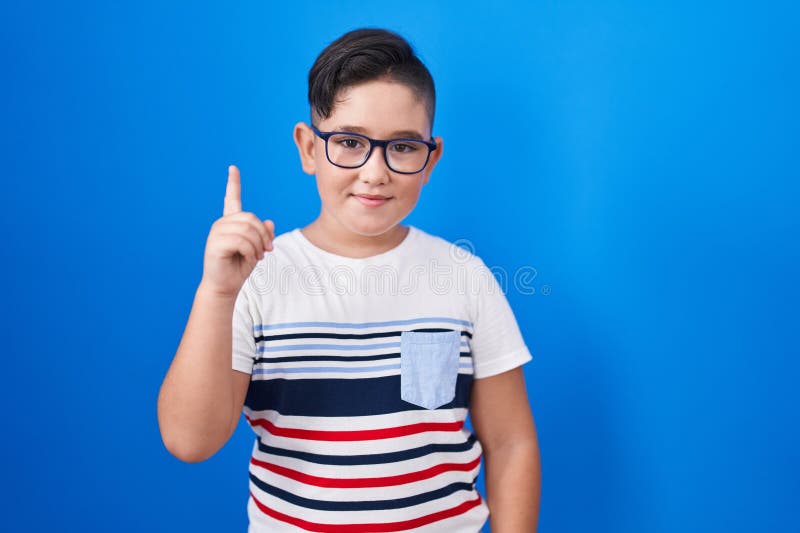 Giovane ispanico sullo sfondo blu che mostra e punta con il dito al primo posto sorridendo sicuro e felice fotografia stock libera da diritti