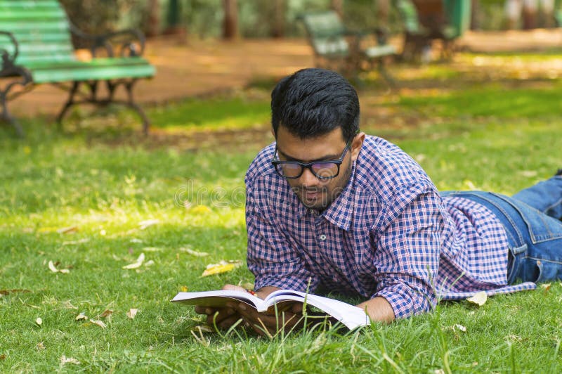 Giovane lettura bella del ragazzo mentre trovandosi nel parco immagini stock libere da diritti Giovane lettura bella del ragazzo mentre trovandosi nel parco immagini stock libere da diritti