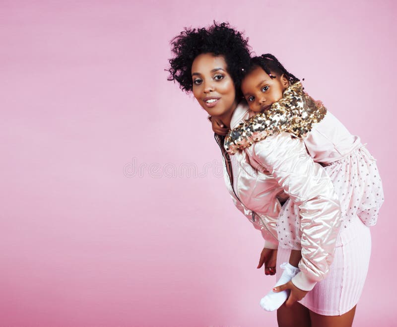 Young pretty african-american mother with little cute daughter hugging, happy smiling on pink background, lifestyle modern people concept closeup. Young pretty african-american mother with little cute daughter hugging, happy smiling on pink background, lifestyle modern people concept closeup