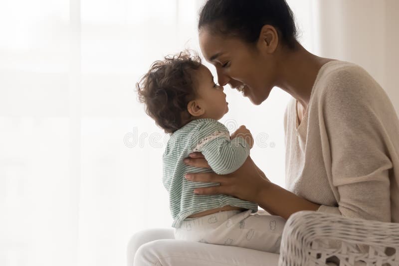 Giovane madre afro-americana sorridente che tocca il naso con un ragazzino carino.