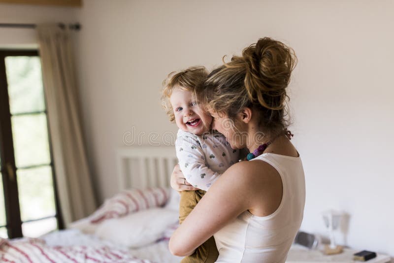 Giovane madre a casa che tiene il suo piccolo figlio sveglio fotografia stock libera da diritti Giovane madre a casa che tiene il suo piccolo figlio sveglio fotografia stock libera da diritti