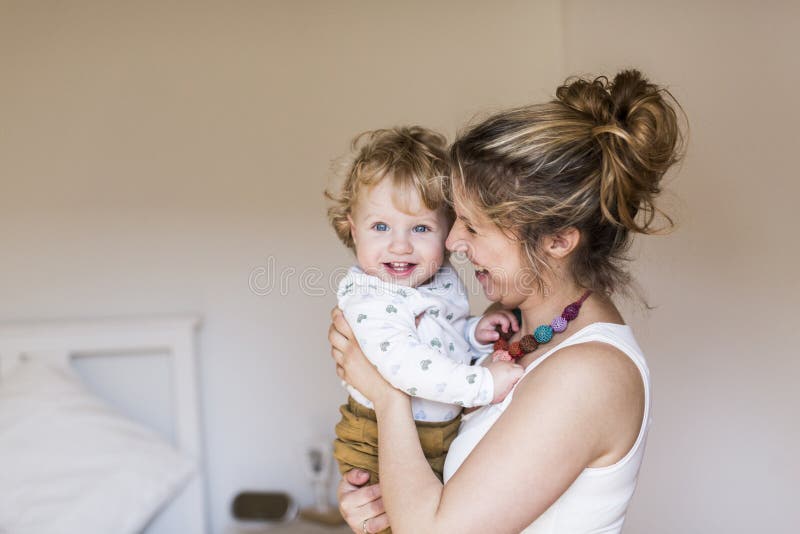 Giovane madre a casa che tiene il suo piccolo figlio sveglio fotografia stock libera da diritti Giovane madre a casa che tiene il suo piccolo figlio sveglio fotografia stock libera da diritti