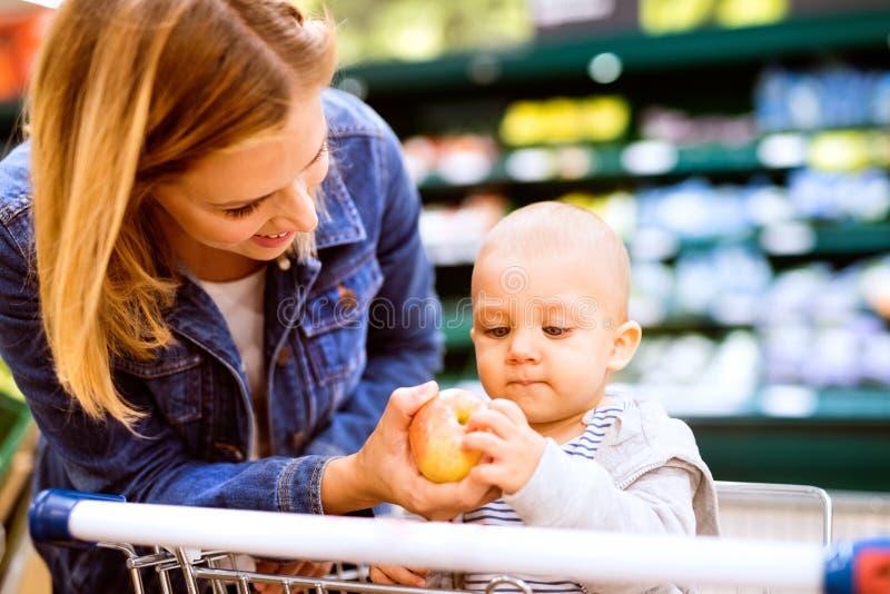 Beautiful young mother with her little baby boy at the supermarket, shopping. Woman giving her son an apple. Close up. Beautiful young mother with her little baby boy at the supermarket, shopping. Woman giving her son an apple. Close up.