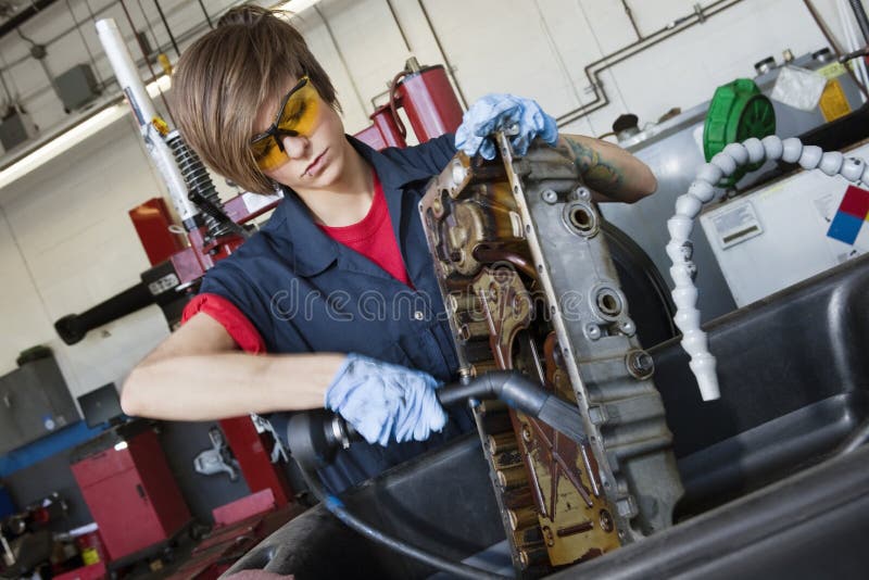 Giovane meccanico femminile che lavora con il cannello per saldare sul pezzo meccanico del veicolo nell'officina riparazioni autom