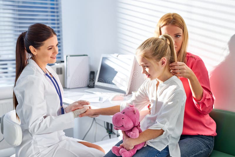 Giovane medico caucasico amico che parla al bambino e alla madre durante il controllo sanitario alla clinica immagini stock libere da diritti