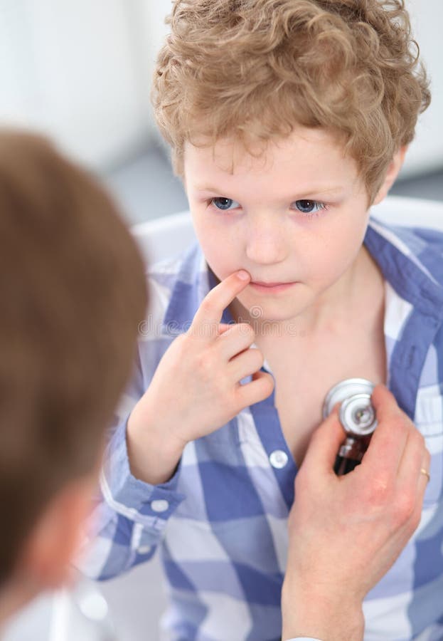 Giovane medico maschio che auscultating un piccolo ragazzo riccio dallo stetoscopio fotografie stock libere da diritti Giovane medico maschio che auscultating un piccolo ragazzo riccio dallo stetoscopio fotografie stock libere da diritti