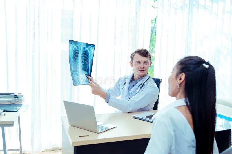 Giovane medico maschio spiega un paziente malato per ascoltare Esame controllando il film della radiografia dell'esame radiografi fotografia stock Giovane medico maschio spiega un paziente malato per ascoltare Esame controllando il film della radiografia dell'esame radiografi fotografia stock