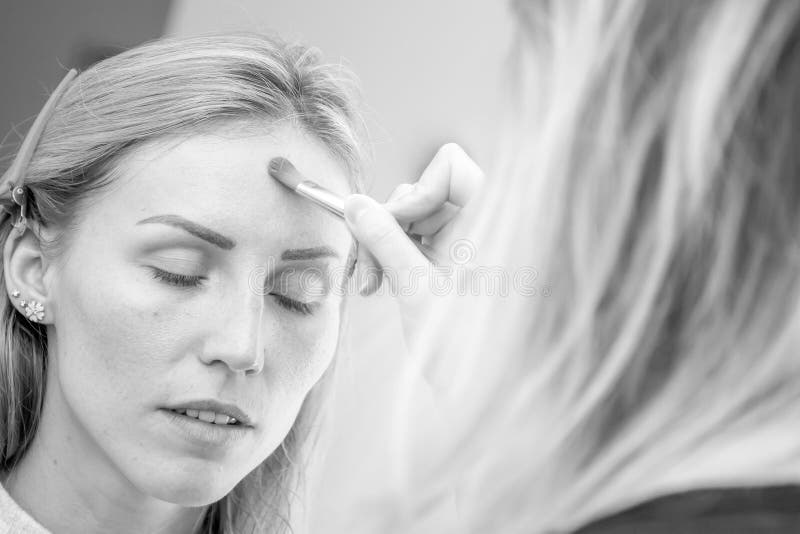 Giovane modello femminile caucasico ad un trucco Stendendo il trucco su a immagine stock Giovane modello femminile caucasico ad un trucco Stendendo il trucco su a immagine stock