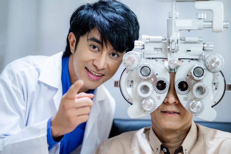 Giovane optometrista maschio con phoropher mentre esamina il paziente fotografie stock libere da diritti