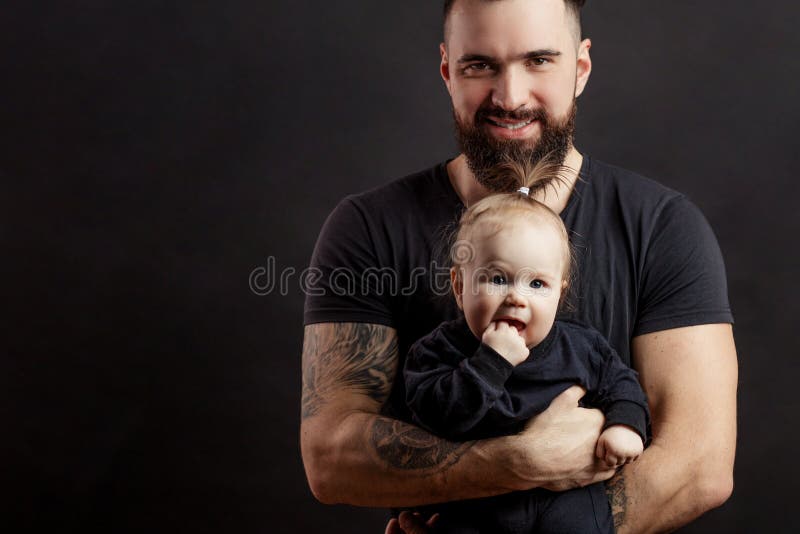 Giovane padre atletico con il bambino adorabile su fondo nero fotografia stock libera da diritti Giovane padre atletico con il bambino adorabile su fondo nero fotografia stock libera da diritti