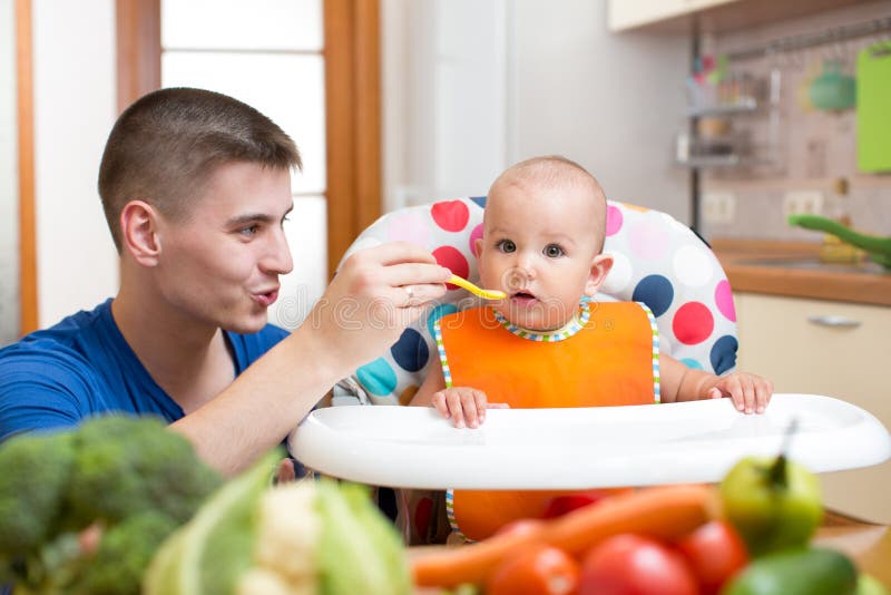 Giovane papà che alimenta il suo bambino alla cucina immagine stock Giovane papà che alimenta il suo bambino alla cucina immagine stock