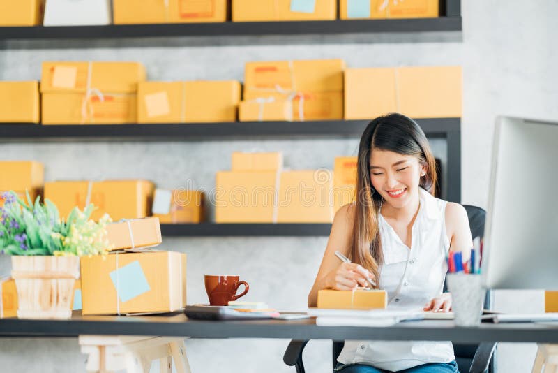 Giovane piccolo imprenditore asiatico che lavora a casa ufficio, prendente nota sugli ordini d'acquisto Consegna d'imballaggio di