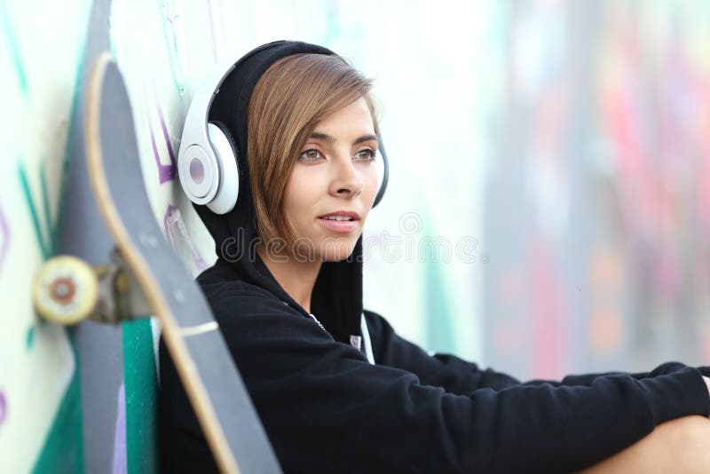 Giovane ragazza del pattinatore che ascolta la musica con le cuffie fotografia stock Giovane ragazza del pattinatore che ascolta la musica con le cuffie fotografia stock