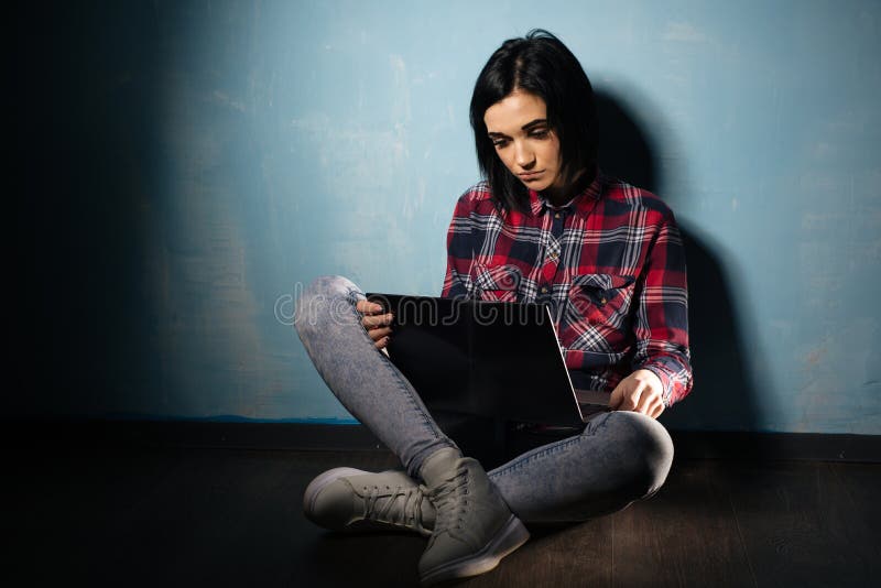 Giovane ragazza triste che soffre dalla dipendenza dalle reti sociali che si siedono sul pavimento con un taccuino fotografia stock libera da diritti Giovane ragazza triste che soffre dalla dipendenza dalle reti sociali che si siedono sul pavimento con un taccuino fotografia stock libera da diritti