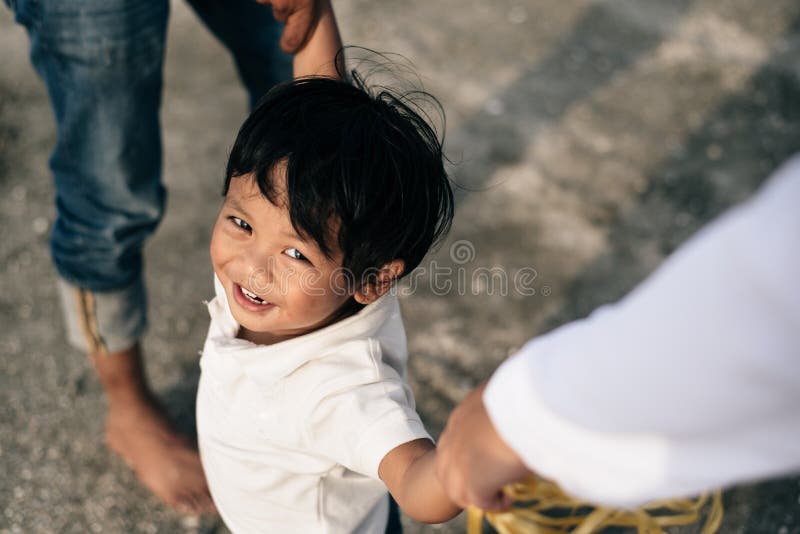 Giovane ragazzo asiatico felice che sorride e che esamina macchina fotografica mentre tenendo la mano del genitore fotografia stock libera da diritti Giovane ragazzo asiatico felice che sorride e che esamina macchina fotografica mentre tenendo la mano del genitore fotografia stock libera da diritti
