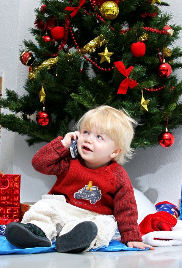 Giovane ragazzo che comunica sul telefono mobile sotto un albero di Natale. fotografia stock libera da diritti