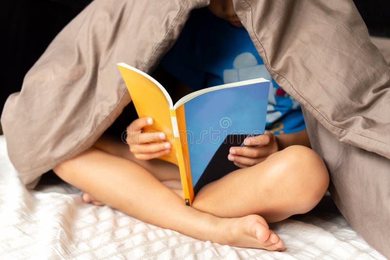 Giovane ragazzo che legge un libro sotto la coperta a letto immagini stock libere da diritti Giovane ragazzo che legge un libro sotto la coperta a letto immagini stock libere da diritti