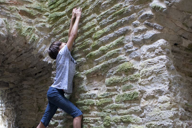 Giovane ragazzo che prova a scalare vecchia parete di pietra immagine stock Giovane ragazzo che prova a scalare vecchia parete di pietra immagine stock