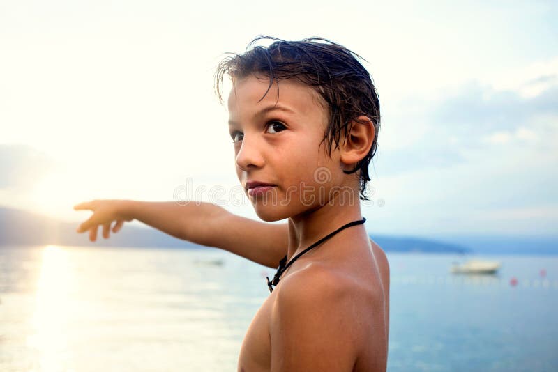Giovane ragazzo che sta indicante nel cielo davanti al mare fotografie stock libere da diritti Giovane ragazzo che sta indicante nel cielo davanti al mare fotografie stock libere da diritti