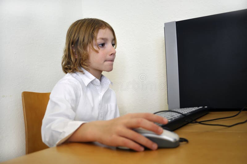 Giovane ragazzo felice che per mezzo di un calcolatore fotografia stock Giovane ragazzo felice che per mezzo di un calcolatore fotografia stock
