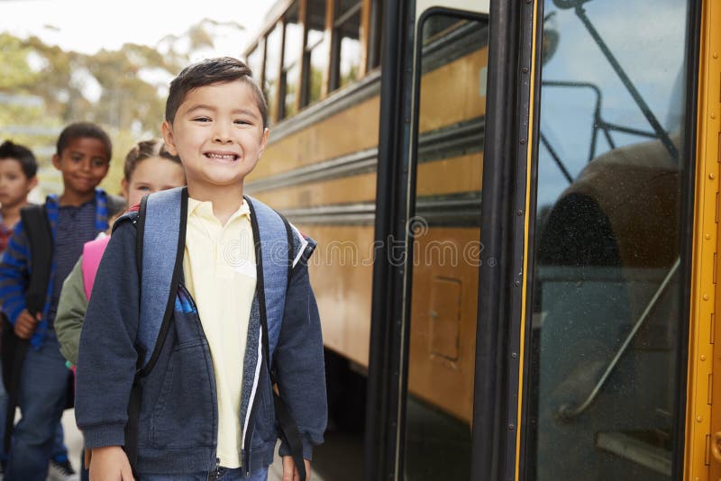 Giovane scolaro ed amici che aspettano per imbarcarsi sullo scuolabus fotografia stock libera da diritti Giovane scolaro ed amici che aspettano per imbarcarsi sullo scuolabus fotografia stock libera da diritti