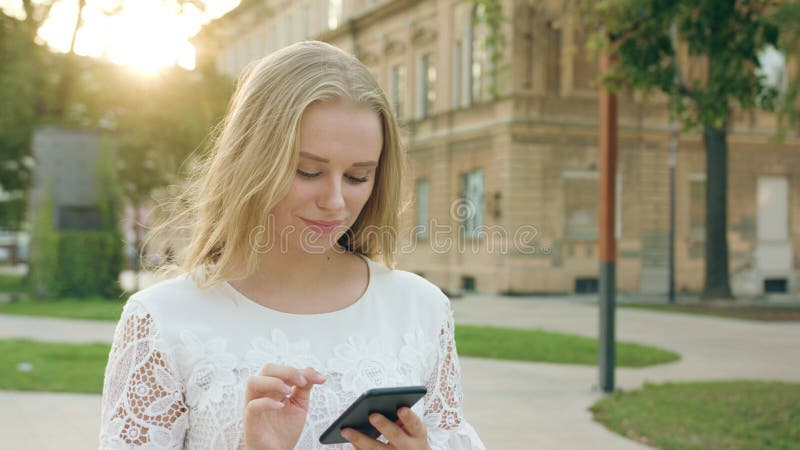 Giovane signora bionda Walking e facendo uso di un telefono in città fotografia stock libera da diritti Giovane signora bionda Walking e facendo uso di un telefono in città fotografia stock libera da diritti