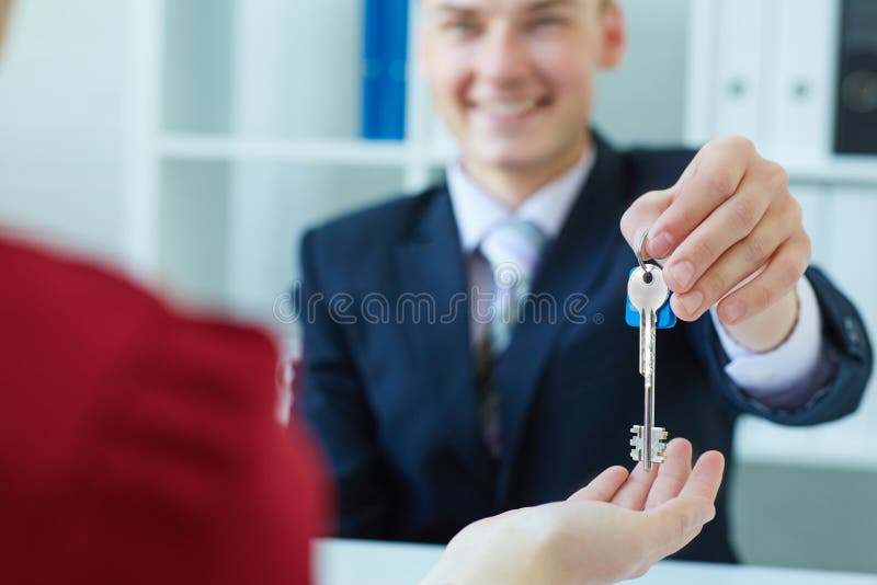 Giovane signora che prende le chiavi dall'agente immobiliare maschio nel corso della riunione immagini stock Giovane signora che prende le chiavi dall'agente immobiliare maschio nel corso della riunione immagini stock