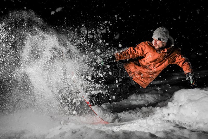 Giovane snowboarder in abiti sportivi arancio che saltano sul bordo alla n fotografia stock Giovane snowboarder in abiti sportivi arancio che saltano sul bordo alla n fotografia stock