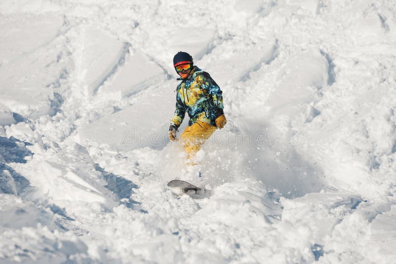 Giovane snowboarder in abiti sportivi luminosi che guidano giù un pendio di montagna della polvere fotografia stock libera da diritti Giovane snowboarder in abiti sportivi luminosi che guidano giù un pendio di montagna della polvere fotografia stock libera da diritti
