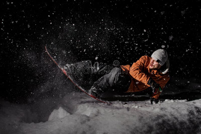 Giovane snowboarder nella guida arancio del rivestimento su una collina nevosa a nig immagine stock Giovane snowboarder nella guida arancio del rivestimento su una collina nevosa a nig immagine stock