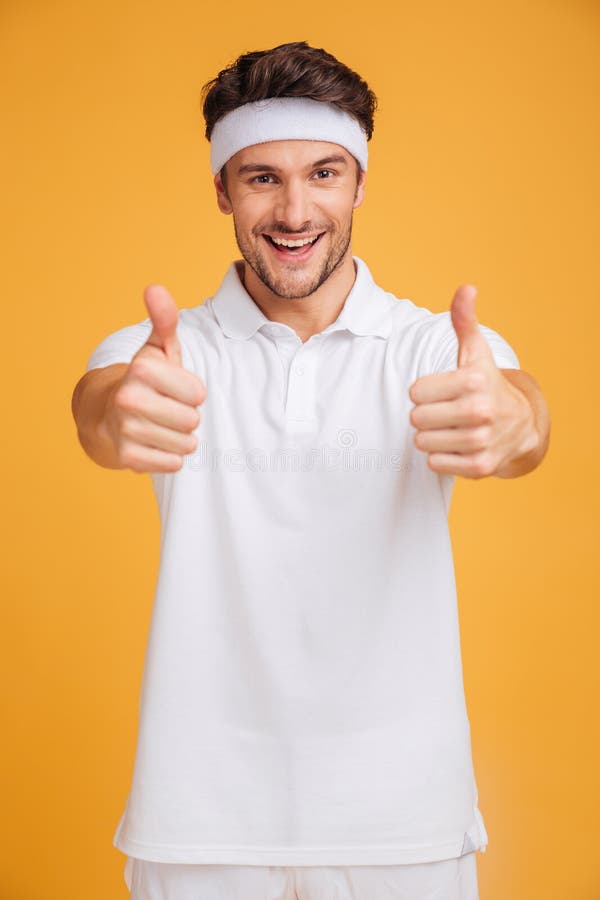 Giovane sportivo bello allegro che mostra i pollici su con entrambe le mani fotografie stock libere da diritti Giovane sportivo bello allegro che mostra i pollici su con entrambe le mani fotografie stock libere da diritti