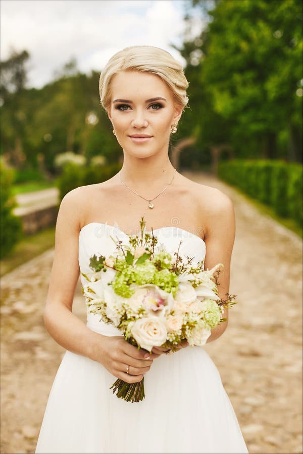 Giovane sposa, bella bionda, ragazza di modello con gli occhi azzurri con i fiori nelle mani, all'aperto fotografia stock libera da diritti Giovane sposa, bella bionda, ragazza di modello con gli occhi azzurri con i fiori nelle mani, all'aperto fotografia stock libera da diritti