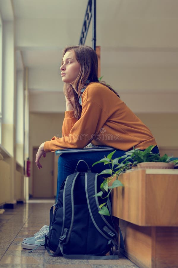 Giovane studente di college femminile solo depresso che si siede nel corridoio alla sua scuola Istruzione, concetto d'oppressione immagine stock Giovane studente di college femminile solo depresso che si siede nel corridoio alla sua scuola Istruzione, concetto d'oppressione immagine stock