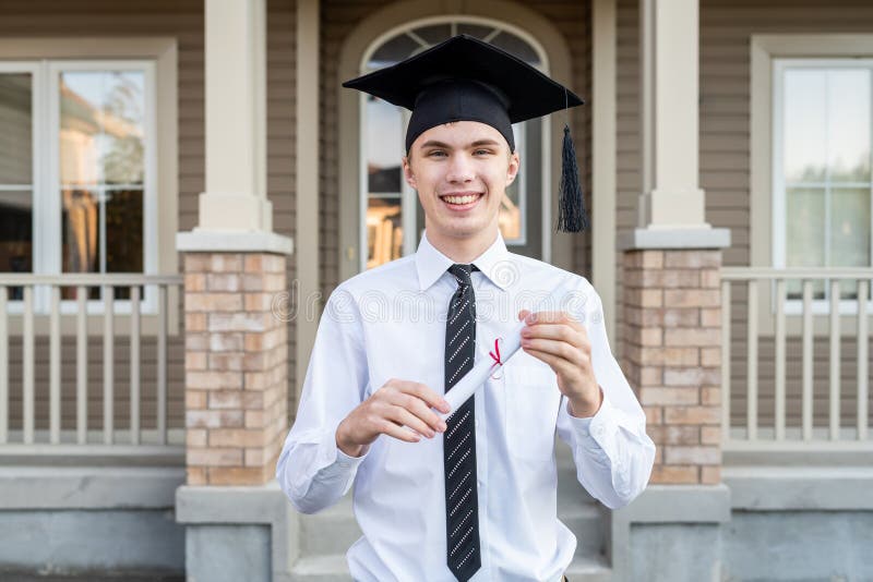 Giovane studente maschio che tiene un diploma mentre indossando un cappuccio di graduazione davanti ad una casa fotografia stock libera da diritti Giovane studente maschio che tiene un diploma mentre indossando un cappuccio di graduazione davanti ad una casa fotografia stock libera da diritti
