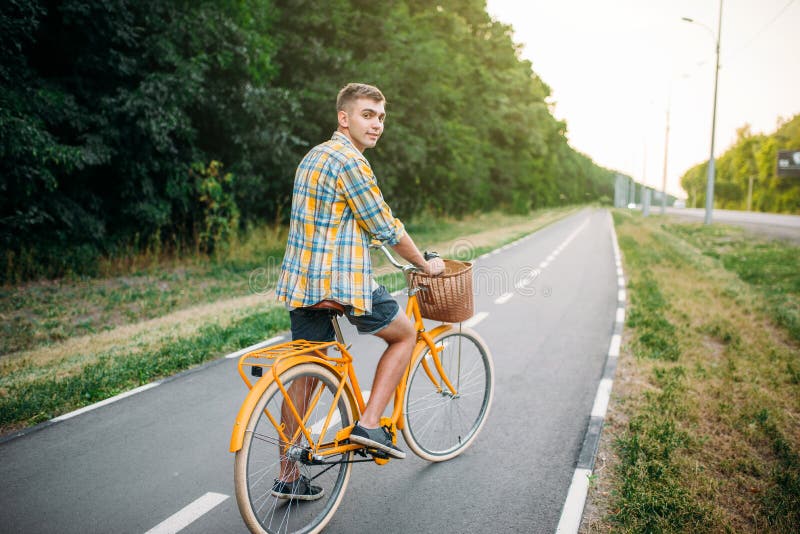 Giovane sulla bicicletta d'annata gialla con il canestro immagine stock Giovane sulla bicicletta d'annata gialla con il canestro immagine stock