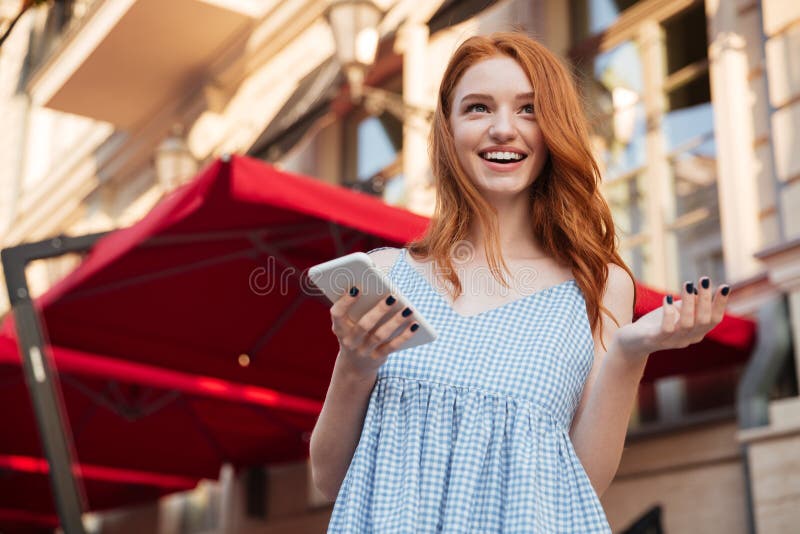 Giovane telefono cellulare emozionante della tenuta della ragazza della testarossa immagine stock Giovane telefono cellulare emozionante della tenuta della ragazza della testarossa immagine stock