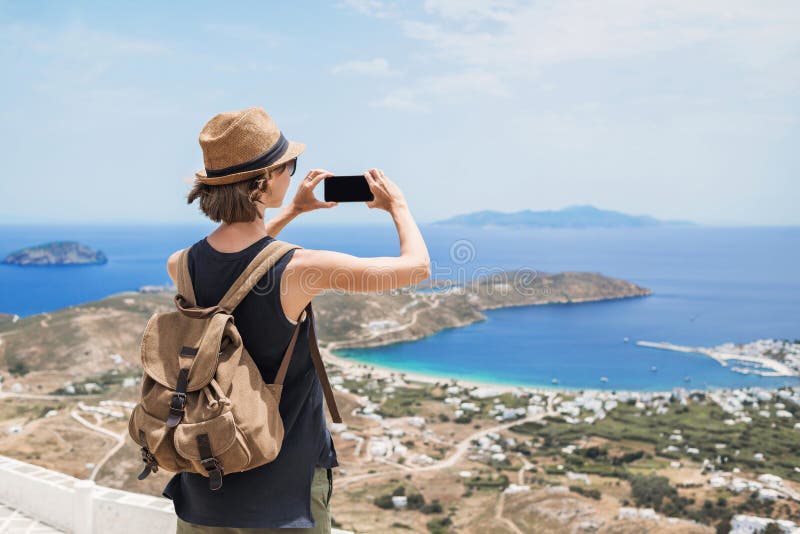 Giovane turista con uno smartphone fotografa un paesaggio bellissimo con il mare in Grecia Ragazza viaggiatrice con zaino e mobil fotografia stock libera da diritti