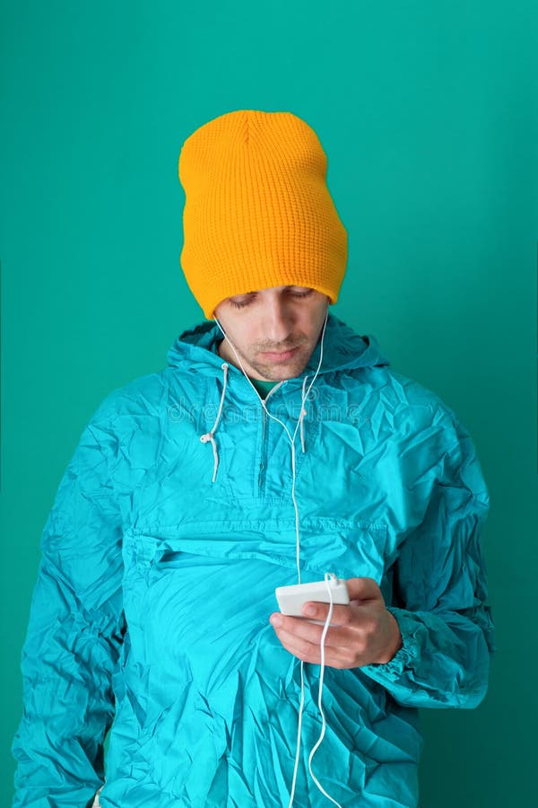 giovane in un rivestimento di stile di sport 90s ed in uno smartphone giallo della tenuta del cappello su un fondo blu immagine stock giovane in un rivestimento di stile di sport 90s ed in uno smartphone giallo della tenuta del cappello su un fondo blu immagine stock
