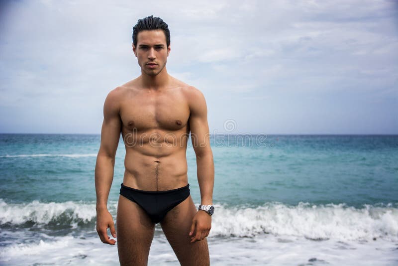 Giovane uomo atletico senza camicia che sta in acqua dalla riva dell'oceano fotografia stock libera da diritti Giovane uomo atletico senza camicia che sta in acqua dalla riva dell'oceano fotografia stock libera da diritti