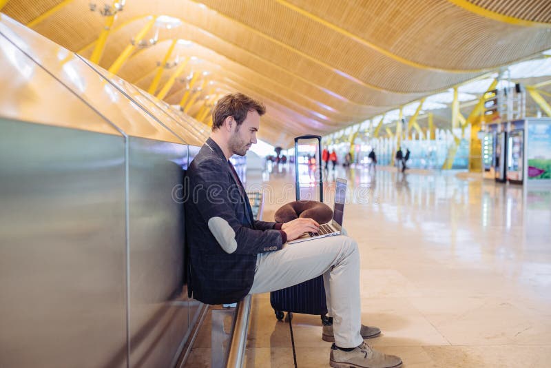 Giovane uomo attraente che si siede all'aeroporto che lavora con un lapto fotografia stock libera da diritti Giovane uomo attraente che si siede all'aeroporto che lavora con un lapto fotografia stock libera da diritti