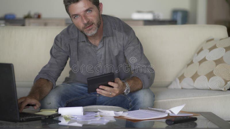 Giovane uomo attraente e felice alle spese dello strato del sofà del salone ed ai pagamenti mensili di stima di debito facendo us immagini stock Giovane uomo attraente e felice alle spese dello strato del sofà del salone ed ai pagamenti mensili di stima di debito facendo us immagini stock