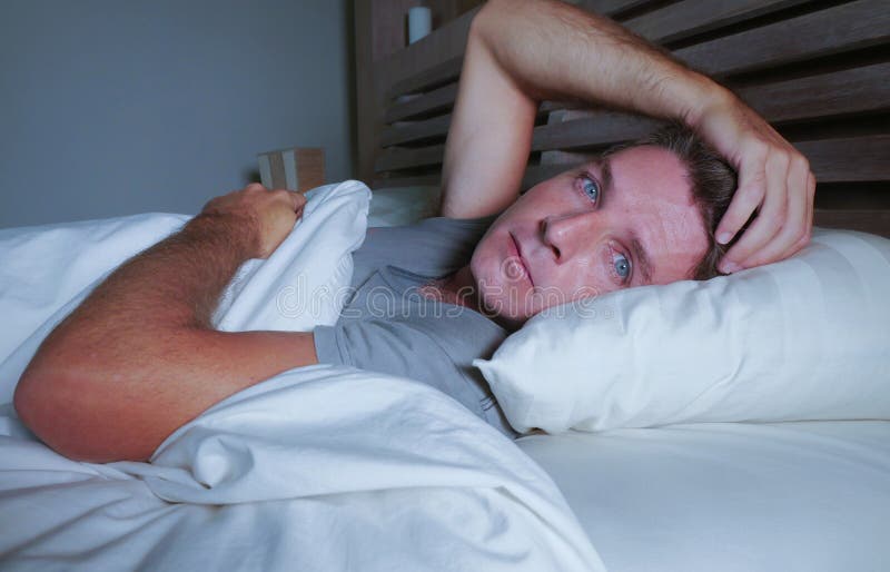 Giovane uomo attraente preoccupato agitato sveglio alla notte che si trova sul letto insonne con l'ampio diso di sofferenza apert fotografia stock Giovane uomo attraente preoccupato agitato sveglio alla notte che si trova sul letto insonne con l'ampio diso di sofferenza apert fotografia stock