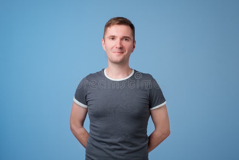 Giovane uomo bello sicuro che tiene armi attraversate e che sorride mentre stando contro il fondo bianco blu immagini stock Giovane uomo bello sicuro che tiene armi attraversate e che sorride mentre stando contro il fondo bianco blu immagini stock