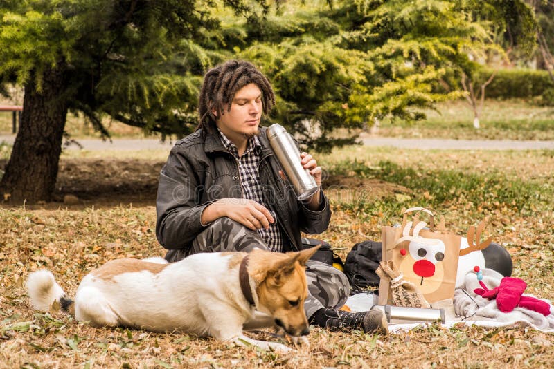 Giovane uomo caucasico divertente con l'acconciatura di afro sul picnic con il suo cane fotografia stock Giovane uomo caucasico divertente con l'acconciatura di afro sul picnic con il suo cane fotografia stock