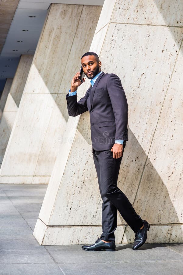 Giovane uomo d'affari afroamericano con la barba che parla sul telefono cellulare fuori dell'ufficio a New York immagini stock libere da diritti Giovane uomo d'affari afroamericano con la barba che parla sul telefono cellulare fuori dell'ufficio a New York immagini stock libere da diritti