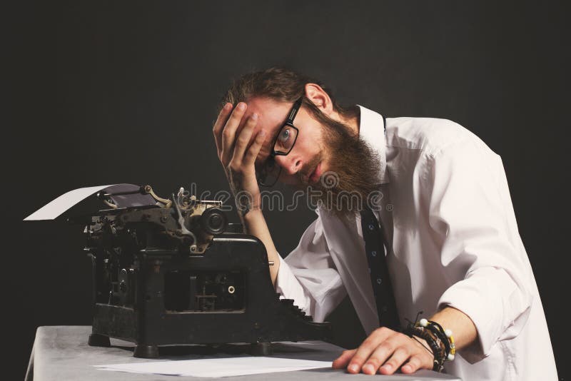Giovane uomo d'affari bello dei pantaloni a vita bassa che pensa e che scrive con la macchina da scrivere d'annata immagine stock Giovane uomo d'affari bello dei pantaloni a vita bassa che pensa e che scrive con la macchina da scrivere d'annata immagine stock