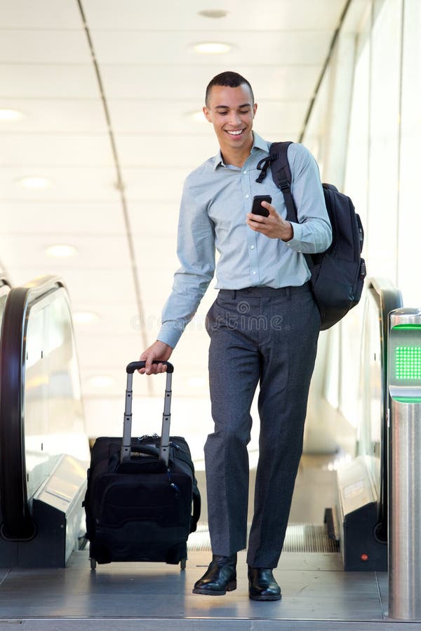 Giovane uomo d'affari dell'ente completo che cammina con le borse ed il telefono cellulare di viaggio fotografia stock Giovane uomo d'affari dell'ente completo che cammina con le borse ed il telefono cellulare di viaggio fotografia stock