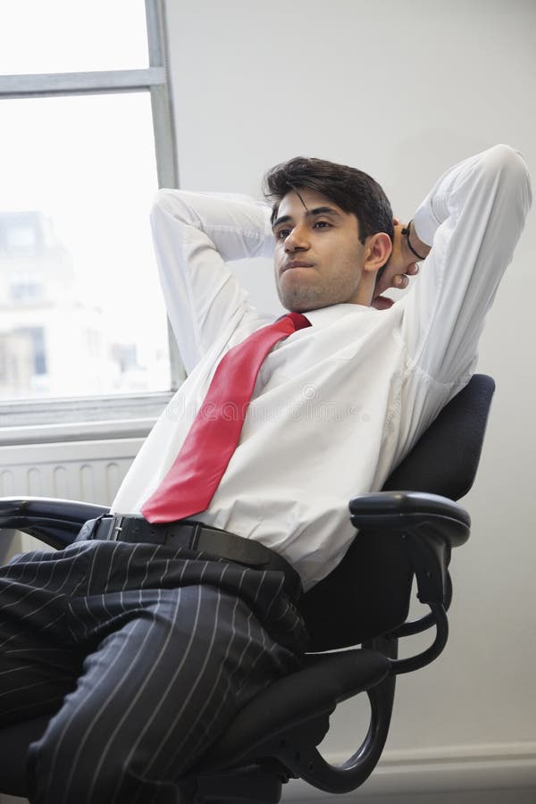 Giovane uomo d'affari indiano che contempla mentre sedendosi nella sedia dell'ufficio fotografia stock Giovane uomo d'affari indiano che contempla mentre sedendosi nella sedia dell'ufficio fotografia stock