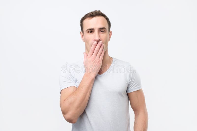 Giovane uomo italiano colpito nella bocca bianca della copertura della maglietta con le mani ed esaminare macchina fotografica immagini stock Giovane uomo italiano colpito nella bocca bianca della copertura della maglietta con le mani ed esaminare macchina fotografica immagini stock
