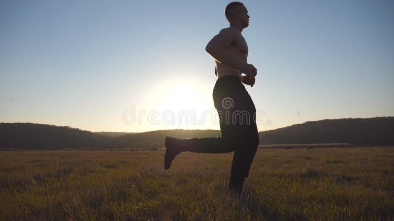 Giovane uomo muscolare che corre attraverso il campo con paesaggi bellissimi sullo sfondo. atleti di sesso maschile. jogging